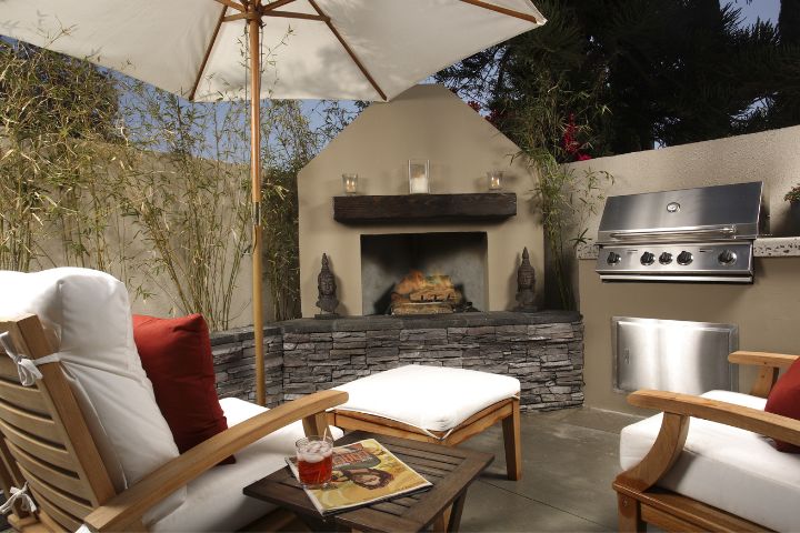 a photo of an outdoor patio with a built in grill, fireplace and lounge chairs showcasing a year-round use of the patio